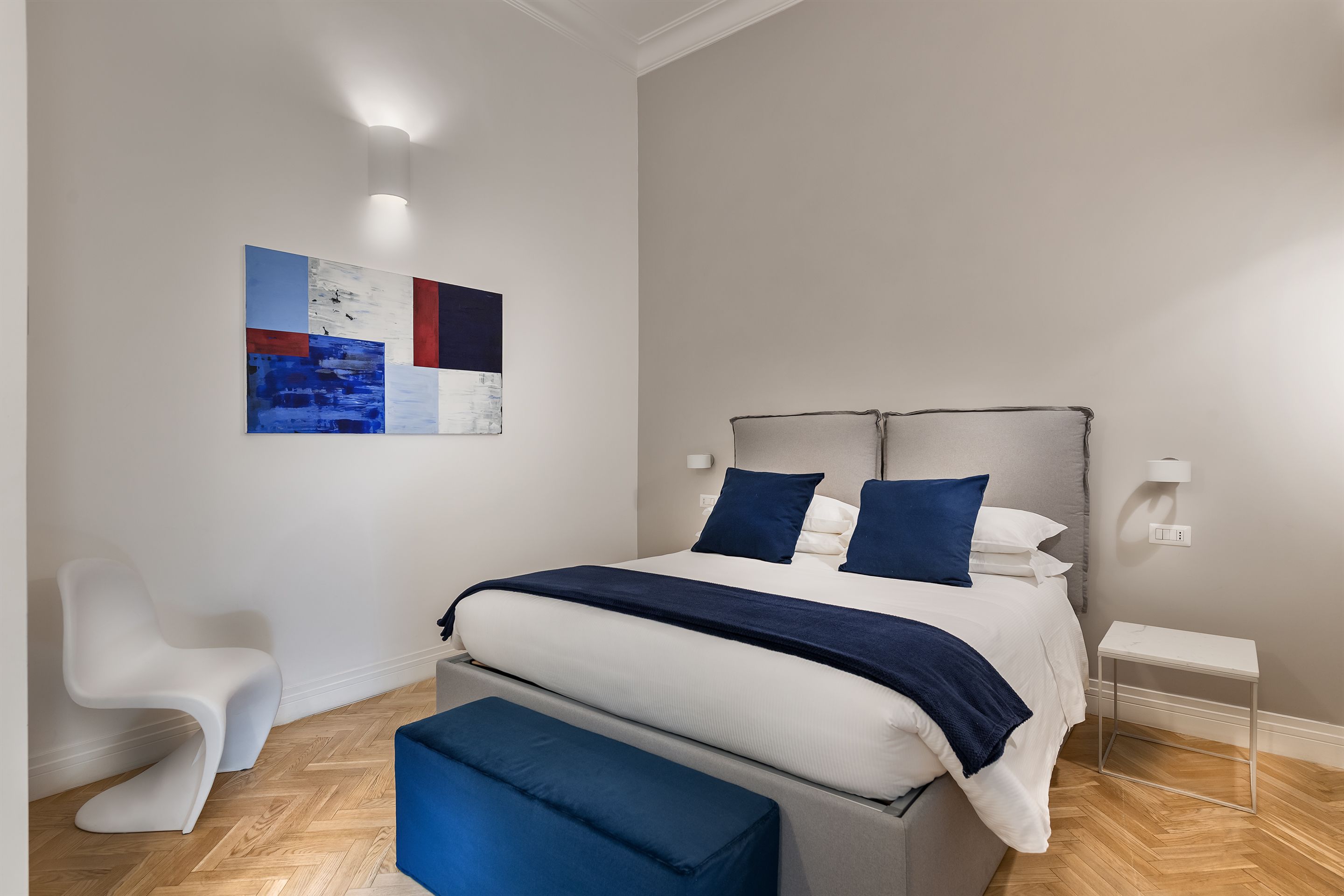 A modern bedroom with a bed, bedside tables, a chair, and a wall art piece.