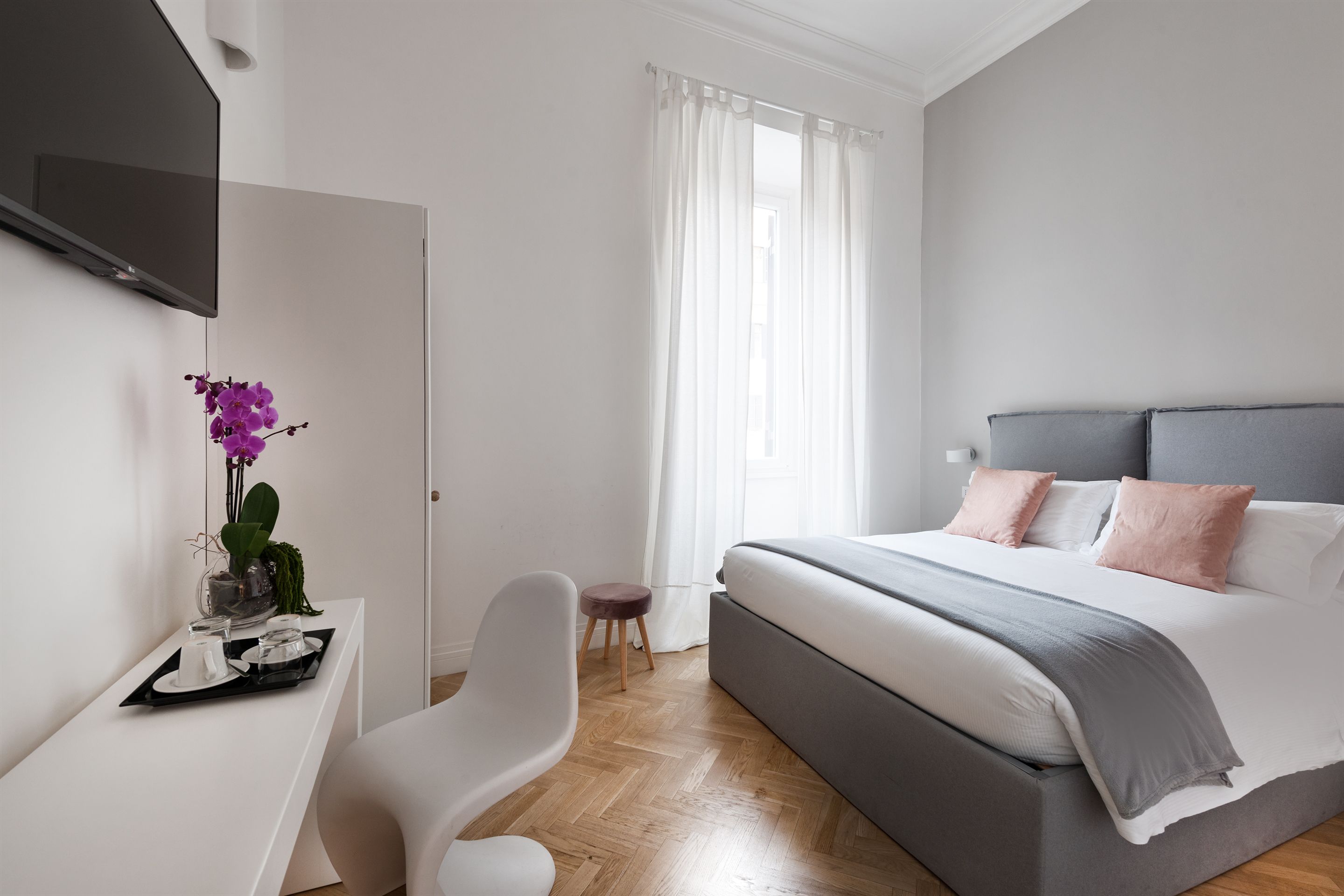 A modern bedroom with a bed, bedside table, chair, and a TV mounted on the wall.