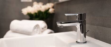 Une salle de bain moderne avec un robinet chromé, un lavabo blanc et une serviette enroulée posée sur le comptoir.