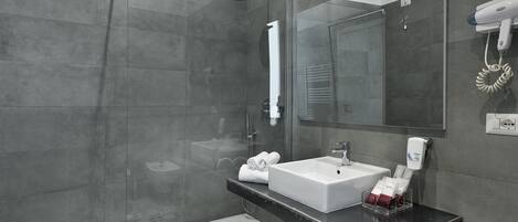 A modern bathroom with a glass-enclosed shower, a white sink, and a hairdryer mounted on the wall.