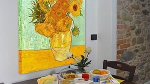 Een eettafel met een schilderij van zonnebloemen, een vaas met bloemen en een dienblad met eten en drinken.