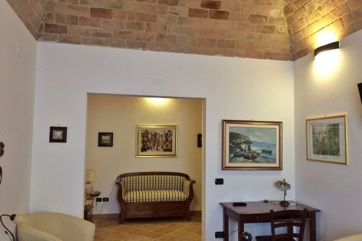 A room with a brick ceiling, a wooden sofa, a small table, and framed artwork on the walls.