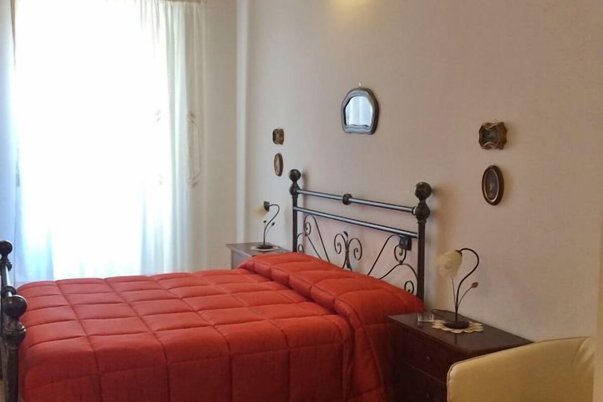 Un dormitorio con cama, mesita de noche, silla y espejo montado en la pared.