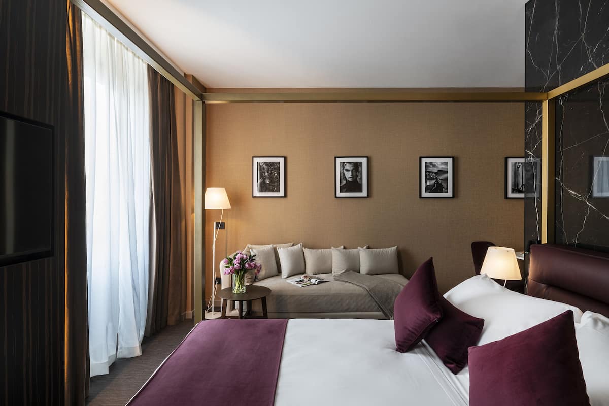 A hotel room with a bed, a sofa, a TV, a lamp, and framed pictures on the wall.