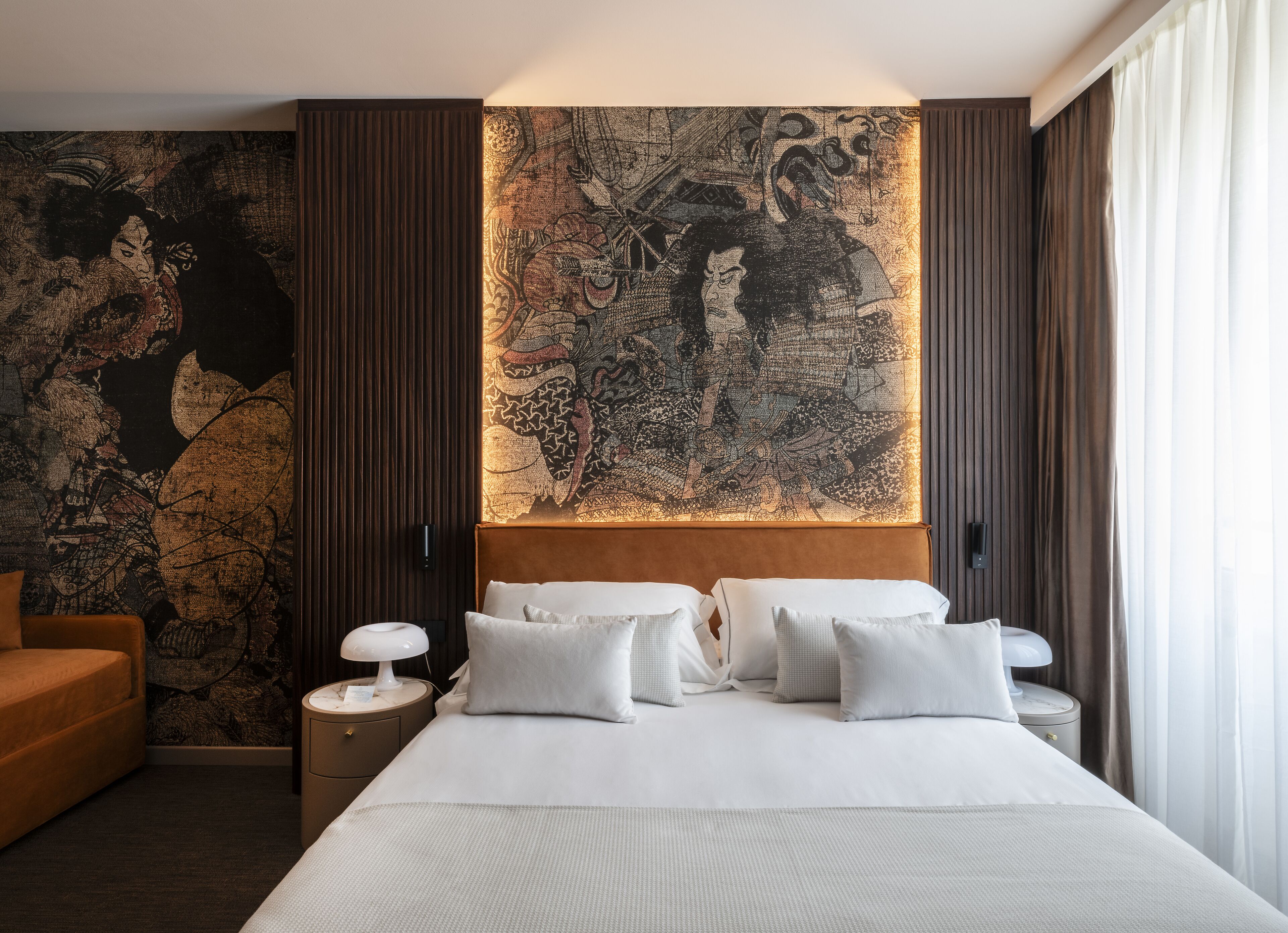 Una camera d'albergo con un letto grande, un comodino, una lampada e una parete decorata con un'opera d'arte di grandi dimensioni.
