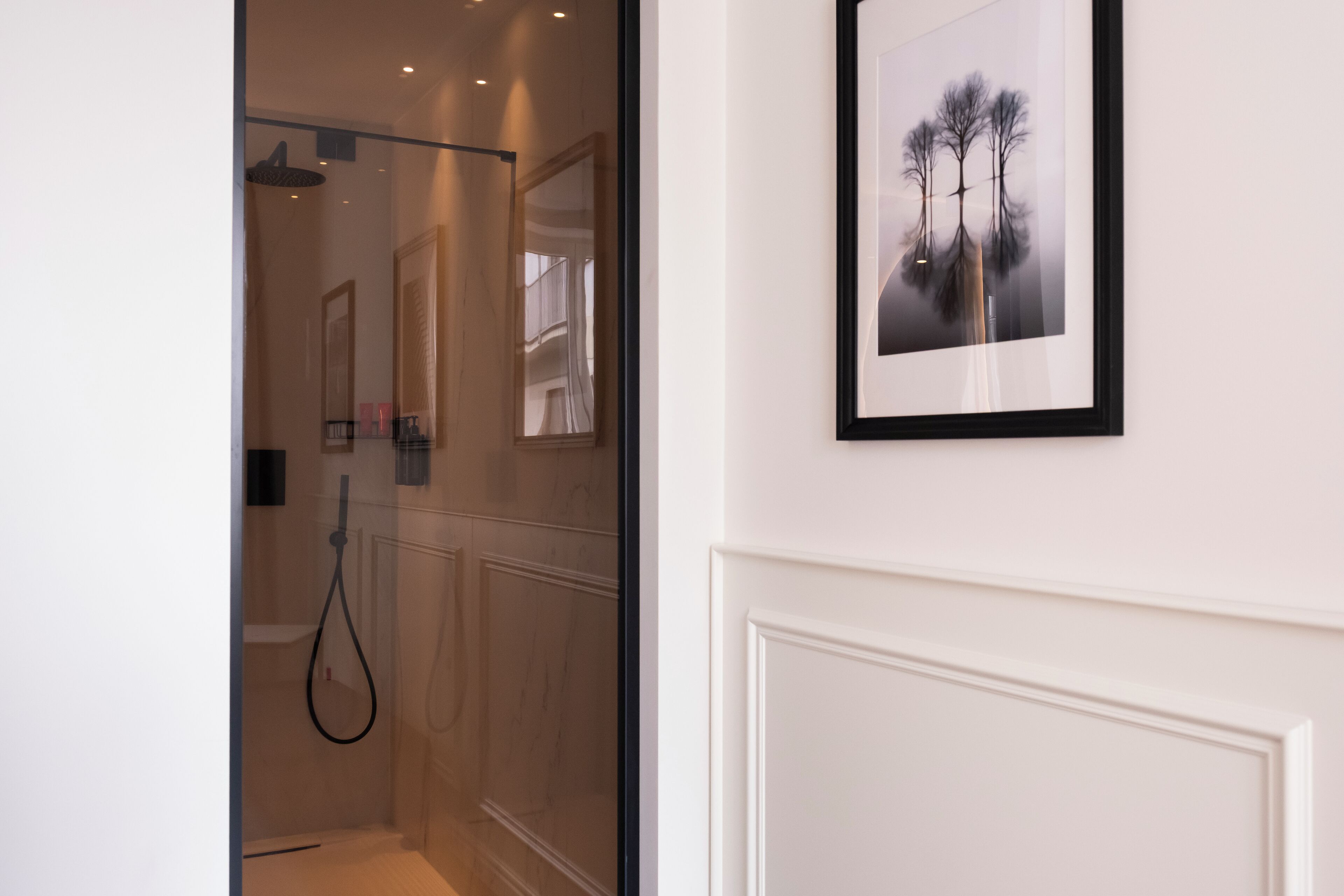 Ein modernes Badezimmer mit Duschkabine aus Glas, einem gerahmten Kunstwerk an der Wand und einer weißen Tür.