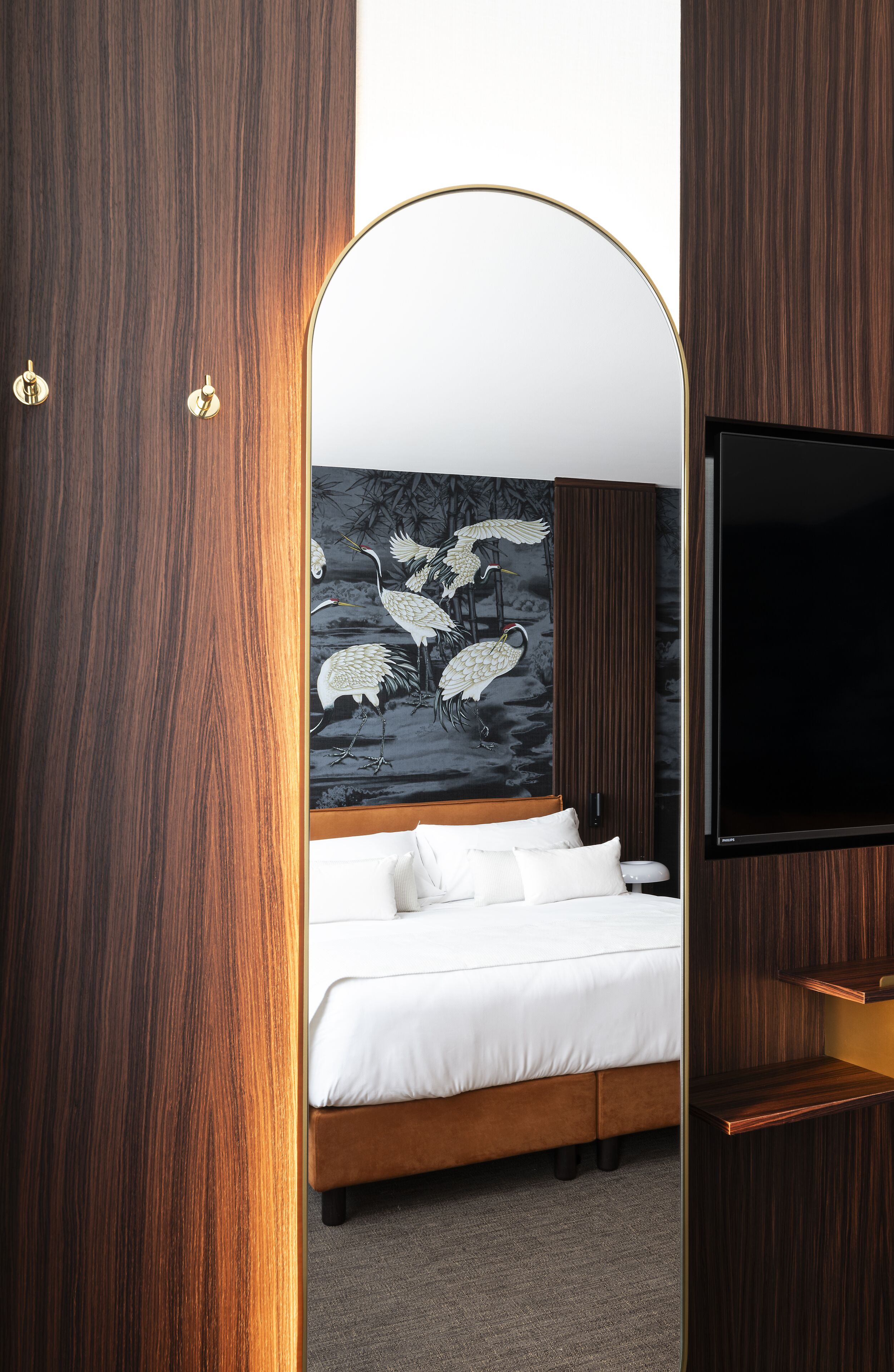 Un dormitorio moderno con piso de madera, una cama grande con ropa blanca, un televisor montado en la pared y un mural de pájaros.