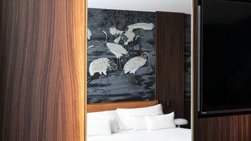 Un dormitorio moderno con piso de madera, una cama grande con ropa blanca, un televisor montado en la pared y un mural de pájaros.