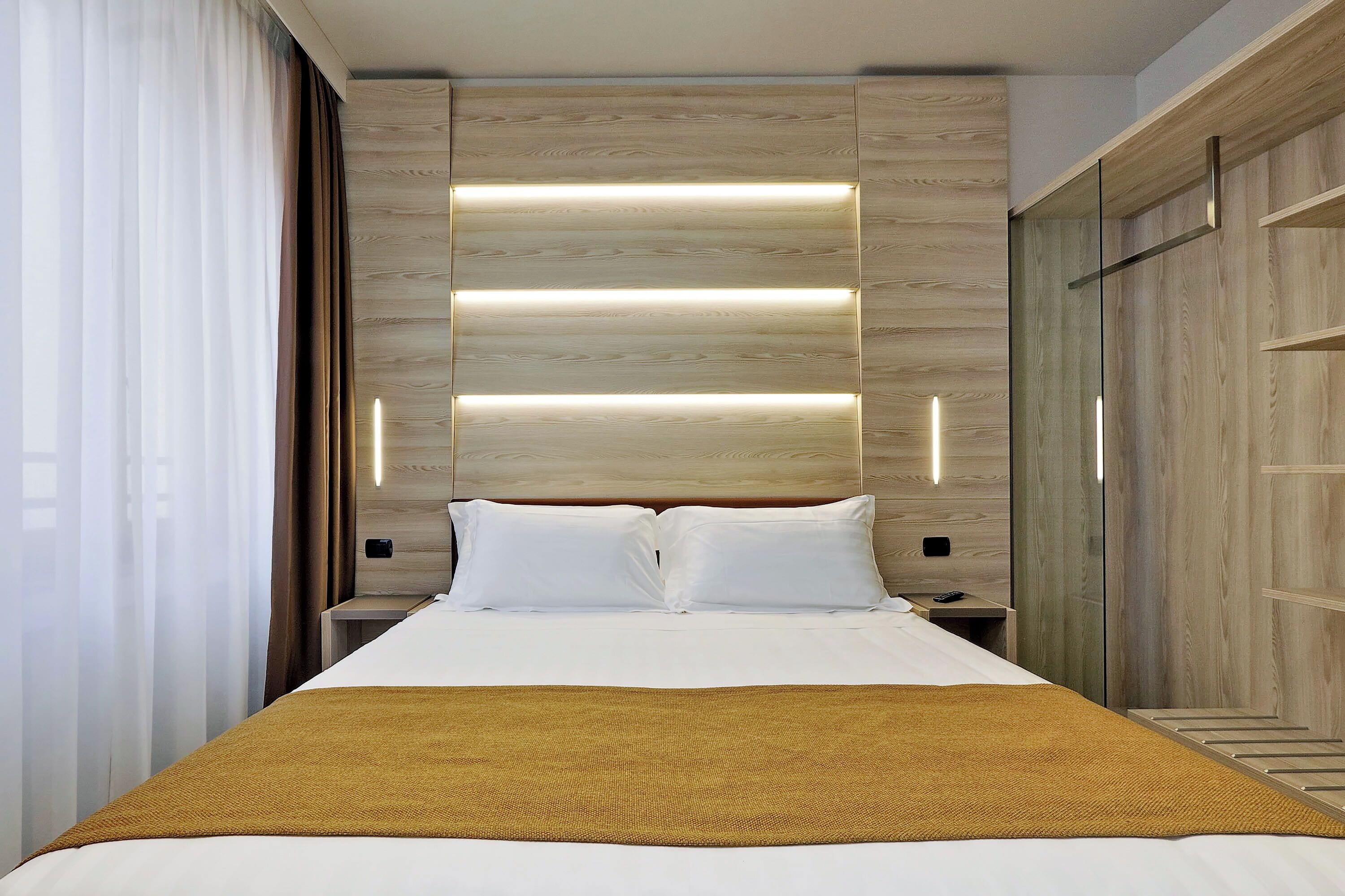 Una camera d'albergo moderna con un grande letto, pannelli in legno alle pareti e un comodino con una lampada.