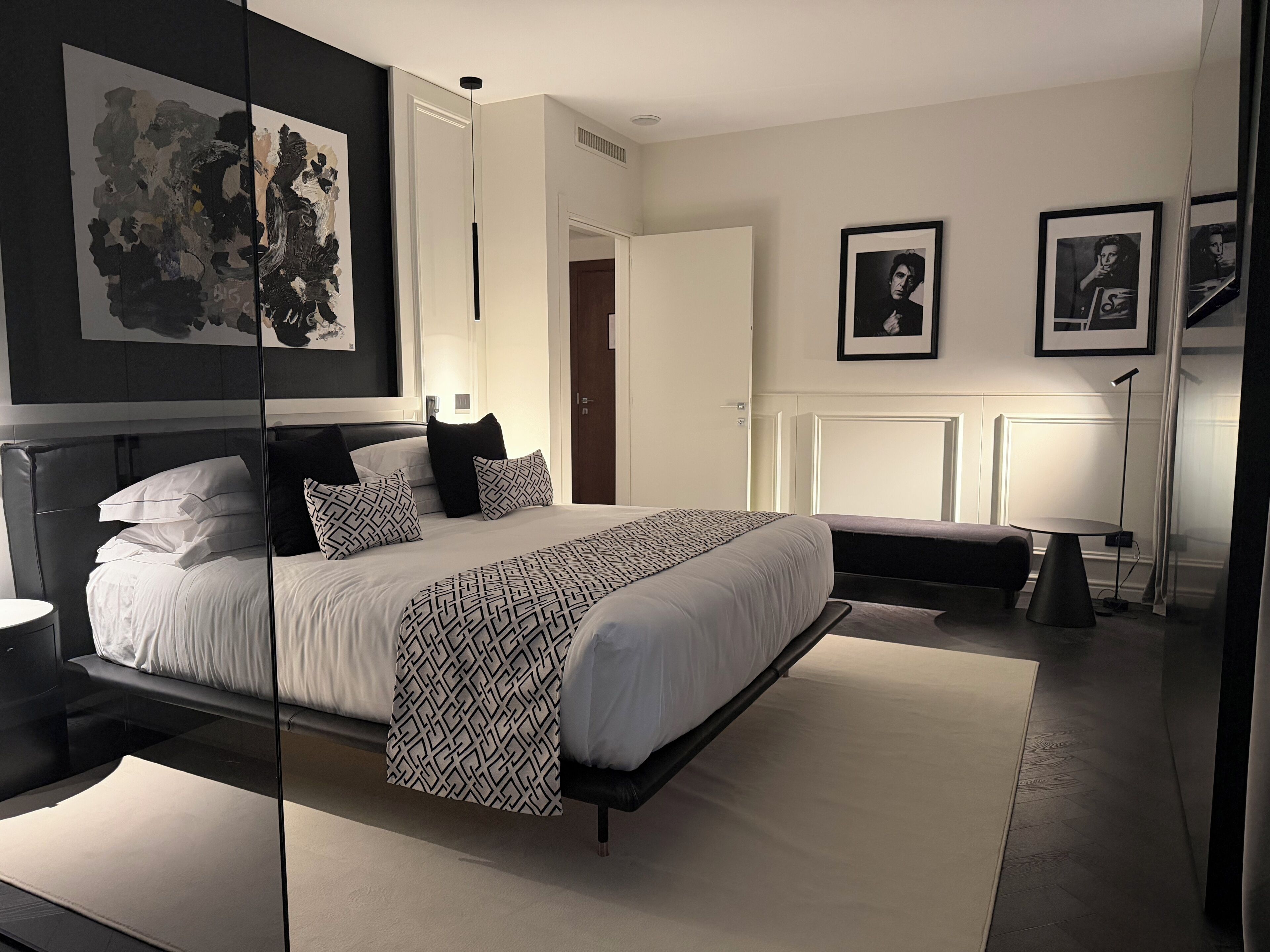 A modern bedroom with a large bed, bedside tables, a reading lamp, and framed pictures on the wall.