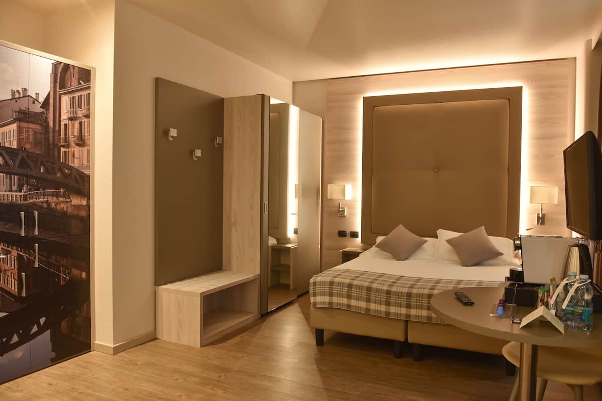 A hotel room with a bed, bedside tables, a desk, and a mirror.