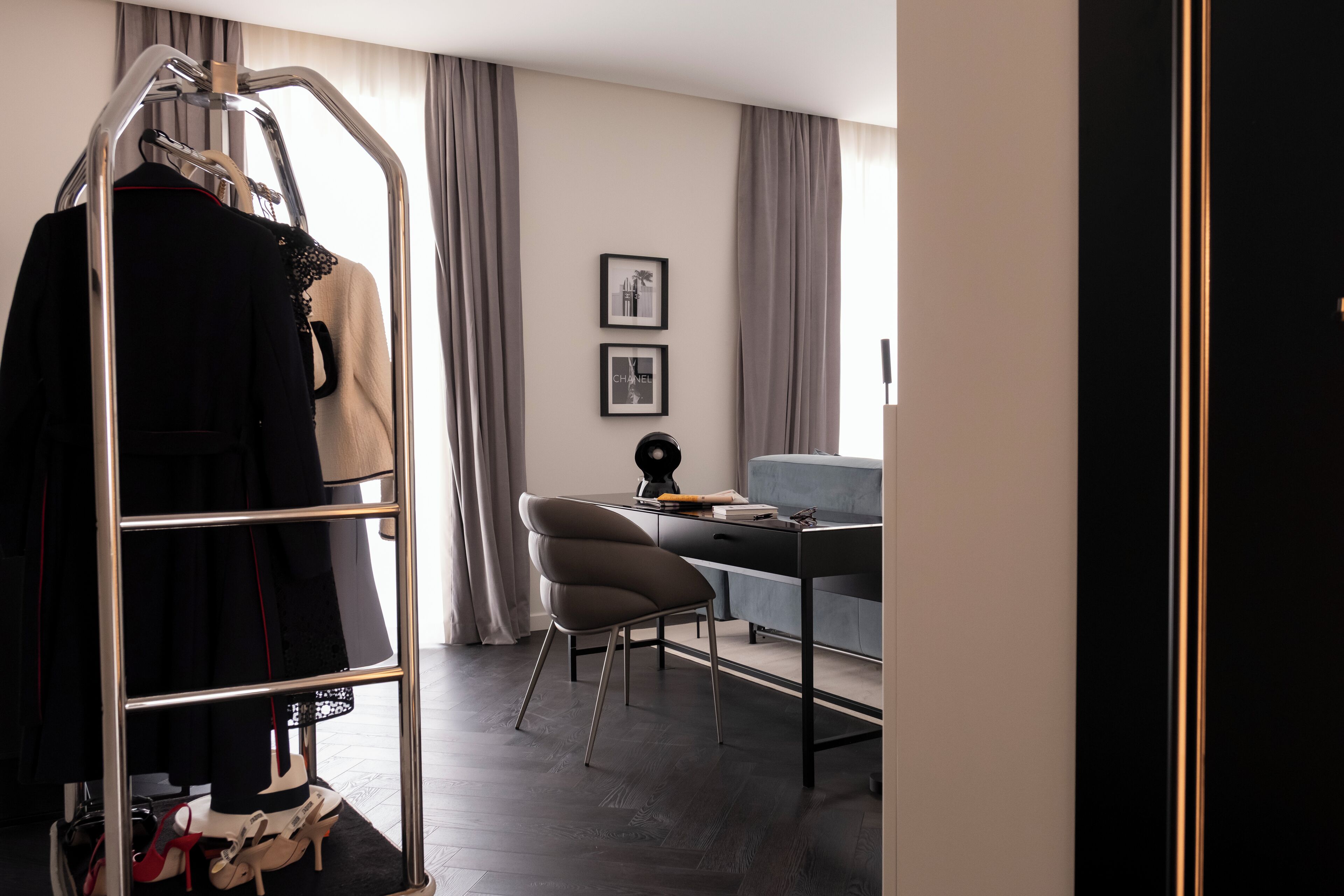 Ein modernes Hotelzimmer mit einem Metallkleiderständer, einem Schreibtisch mit Stuhl und einem Sofa.