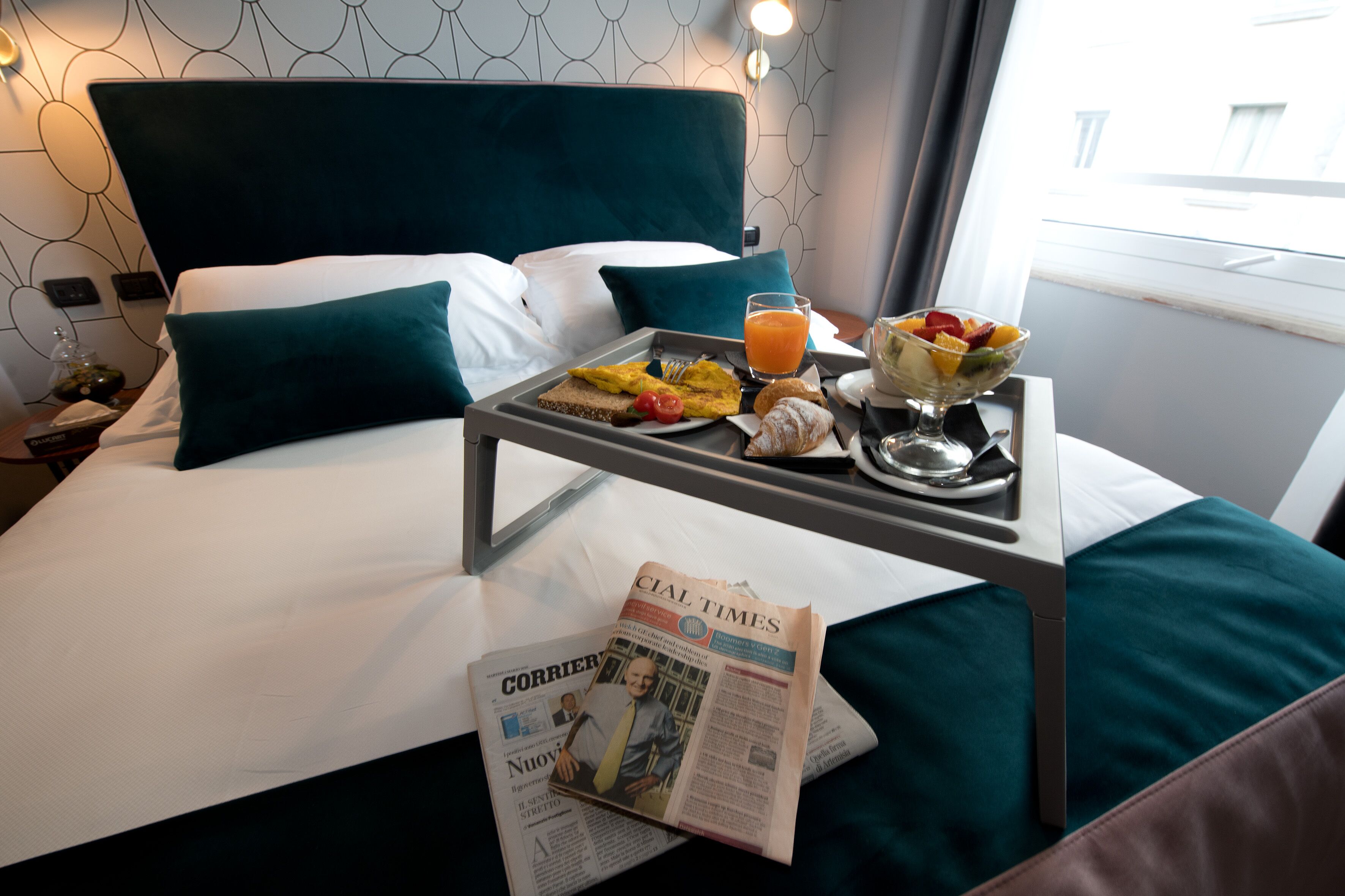 A neatly made bed with a tray of breakfast items, including toast, fruit, and juice, and a newspaper on the bed.