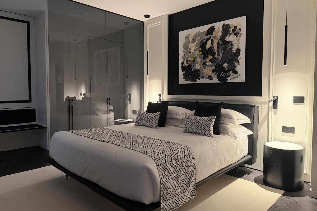 A modern bedroom with a large bed, a glass wardrobe, and a contemporary abstract painting.