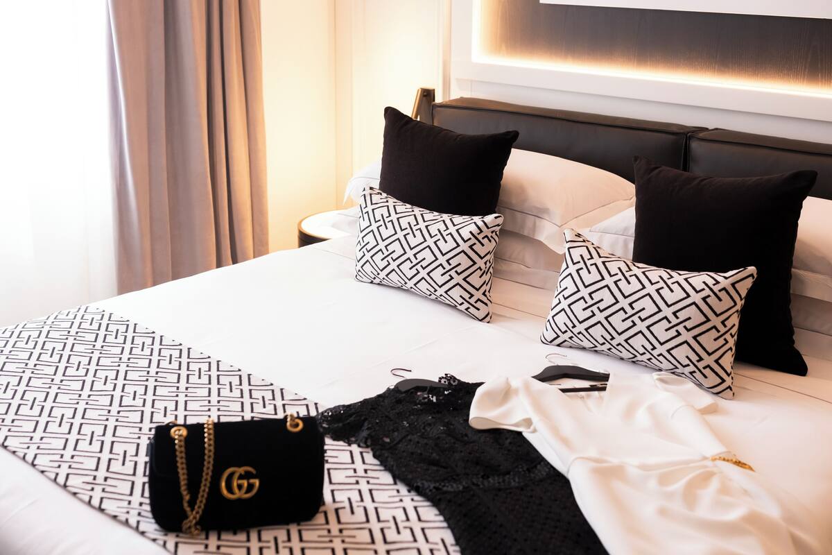 A neatly made bed with patterned pillows and a black and white dress on it.