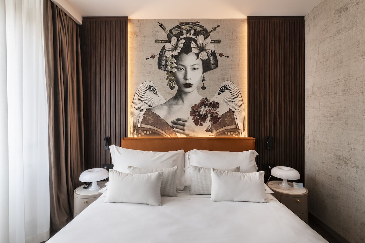 A hotel room with a large bed, white bedding, two bedside tables with lamps, and a large artwork on the wall.