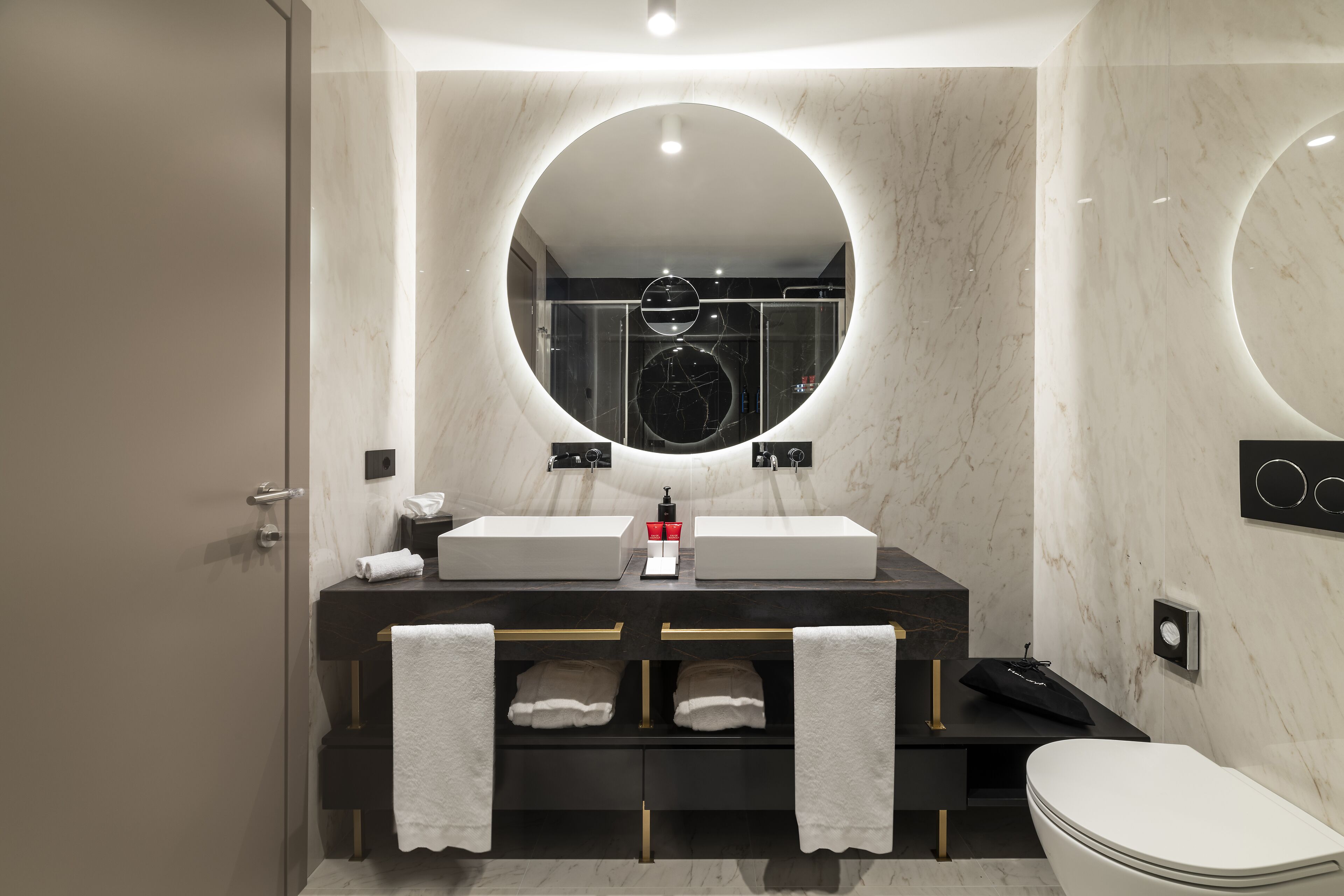 A modern bathroom with a large mirror, two sinks, and a toilet.