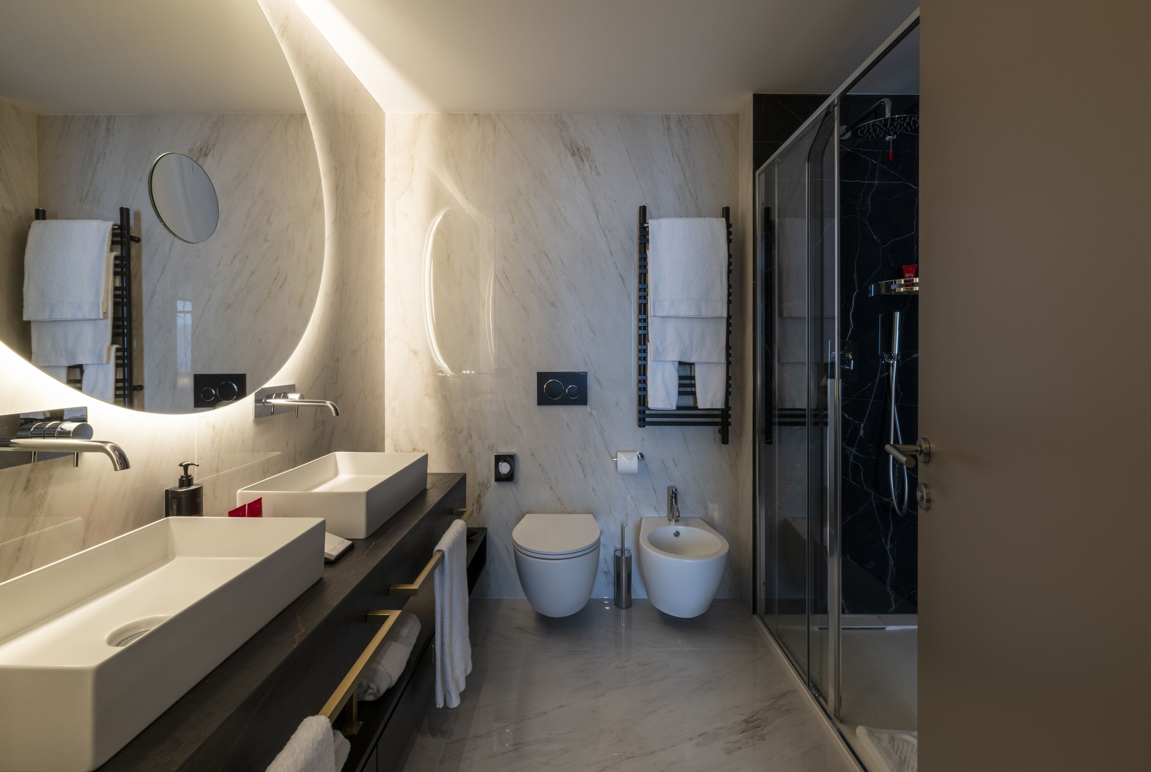 A modern bathroom with two sinks, a toilet, bidet, and a glass shower enclosure.