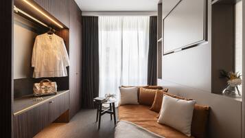 Ein modernes Hotelzimmer mit Bett, Schminktisch mit Spiegel, einem aufhängbaren Bademantel und einem kleinen Tisch mit einer Vase.