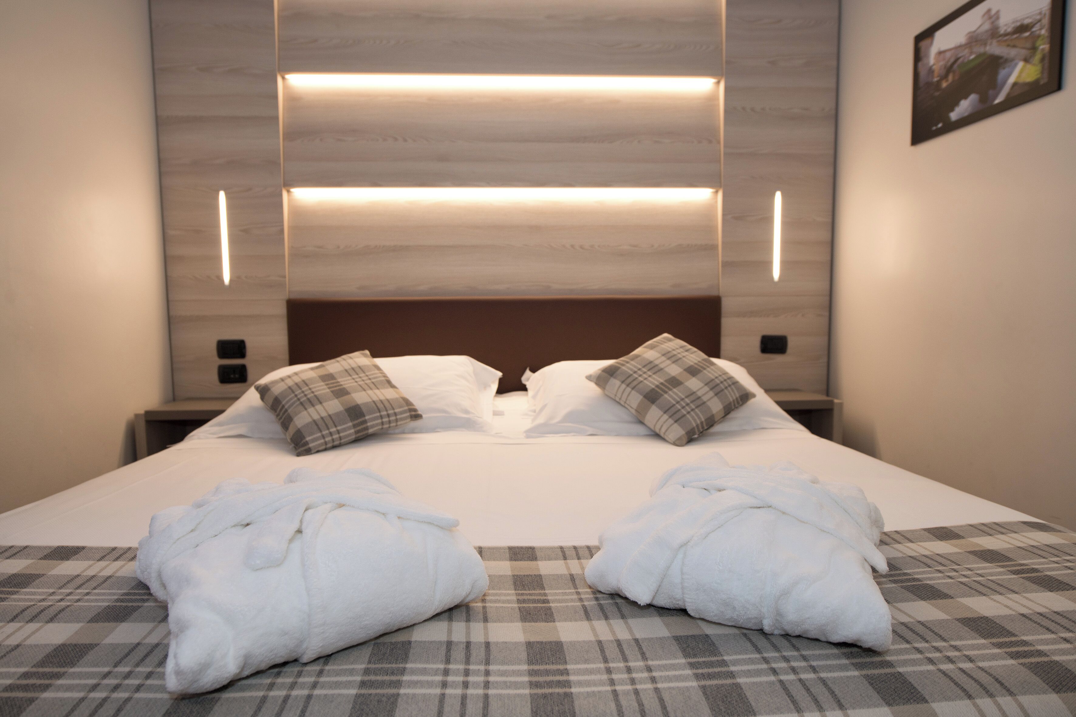 A neatly made bed with two pillows, a checkered blanket, and two towels on the bed.