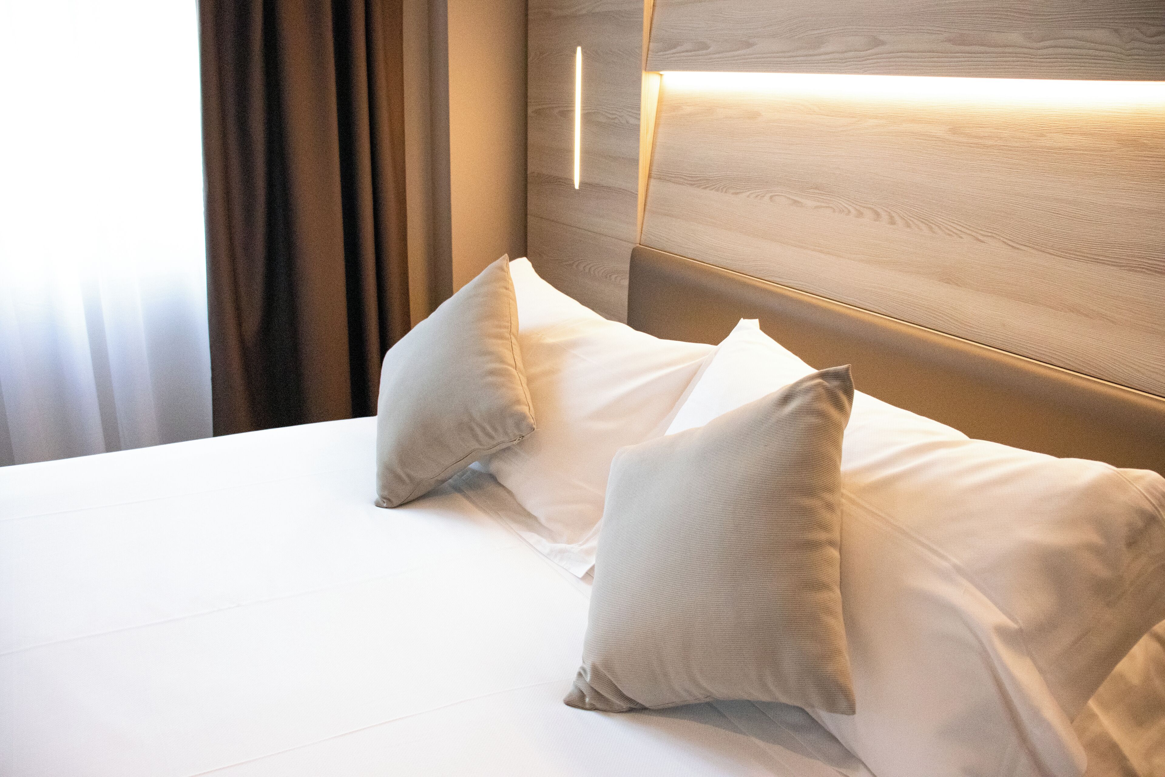 A neatly made bed with white linens and two pillows, a wooden headboard, and a bedside lamp.
