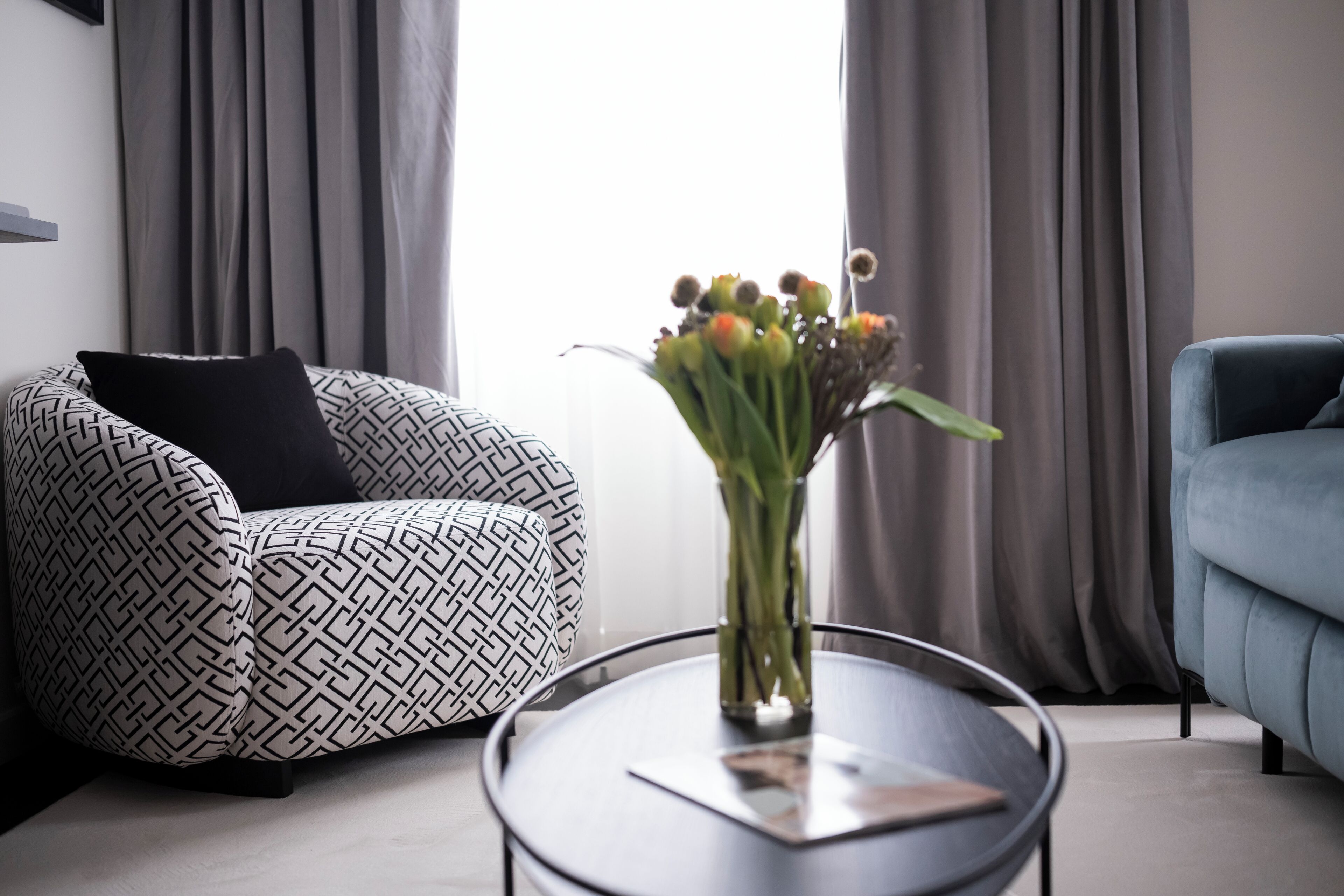 Ein modernes Wohnzimmer mit einem gemusterten Sofa, einem runden Couchtisch und einer Vase mit Blumen.