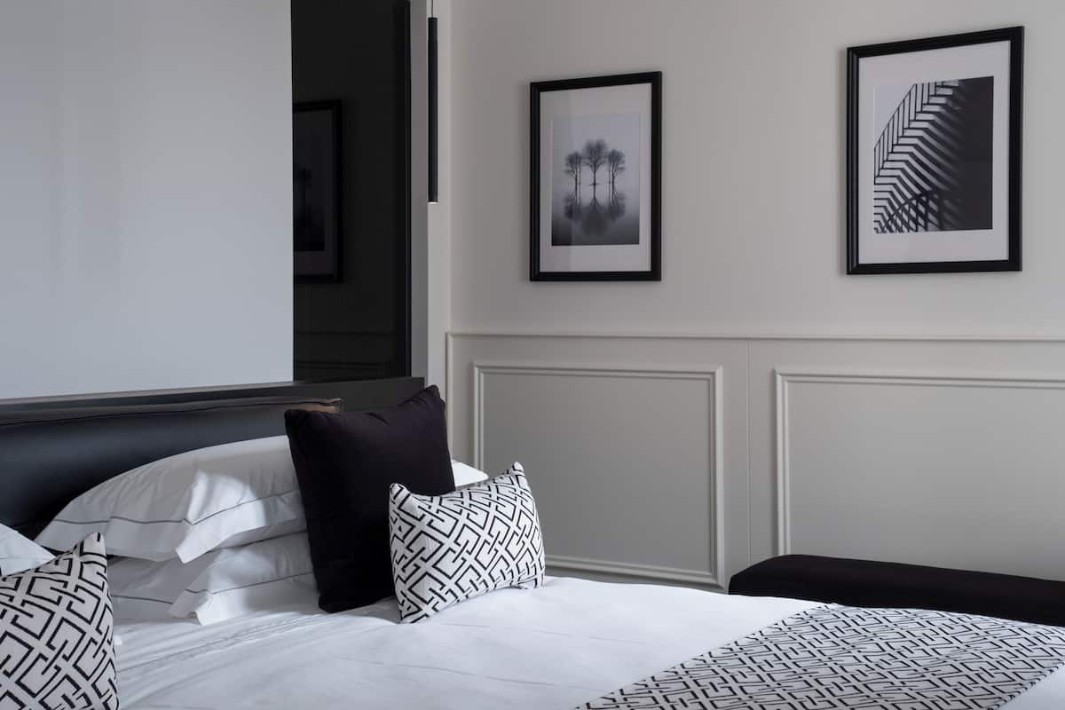 A hotel room with a bed, pillows, and two framed pictures on the wall.