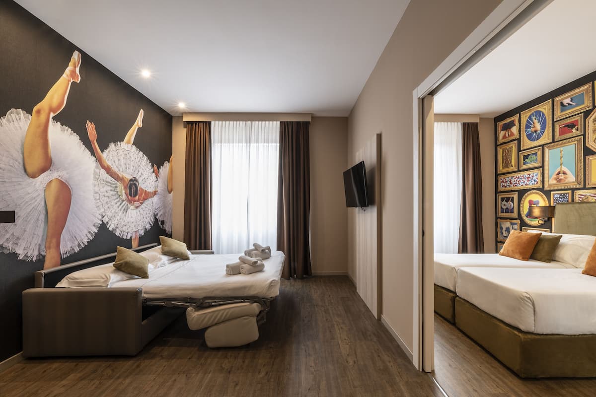 A hotel room with two beds, a large mirror, a flat-screen TV, and a wall with framed pictures.