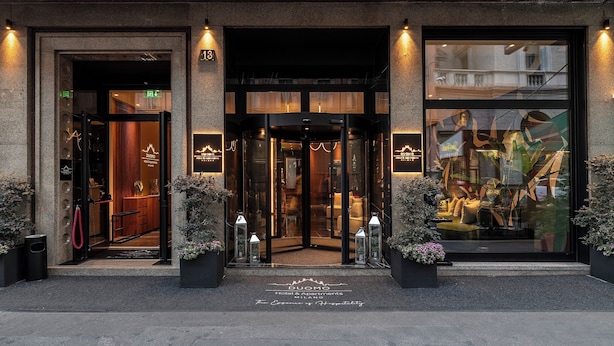 La entrada a un hotel con puerta giratoria, puertas de vidrio y un cartel que indica el nombre 'Duomo Hotel & Apartments'.