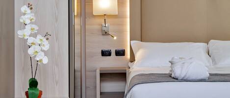 A neatly arranged hotel room with a bed, bedside table, lamp, and a potted orchid.