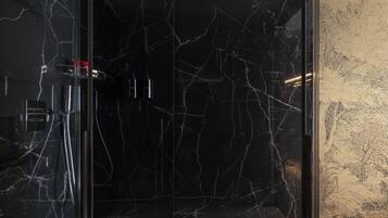 A bathroom with a black marble wall, a glass shower enclosure, and a decorative wall panel.