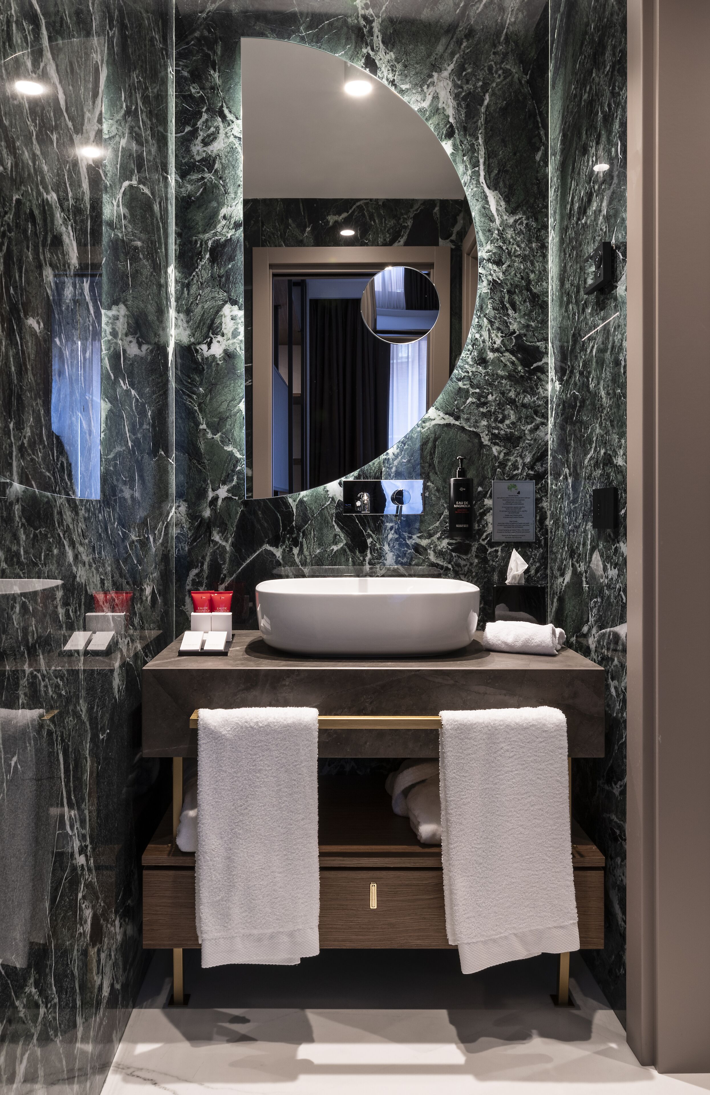 Un baño moderno con un lavamanos ovalado grande, paredes de mármol y un espejo con arco curvo.