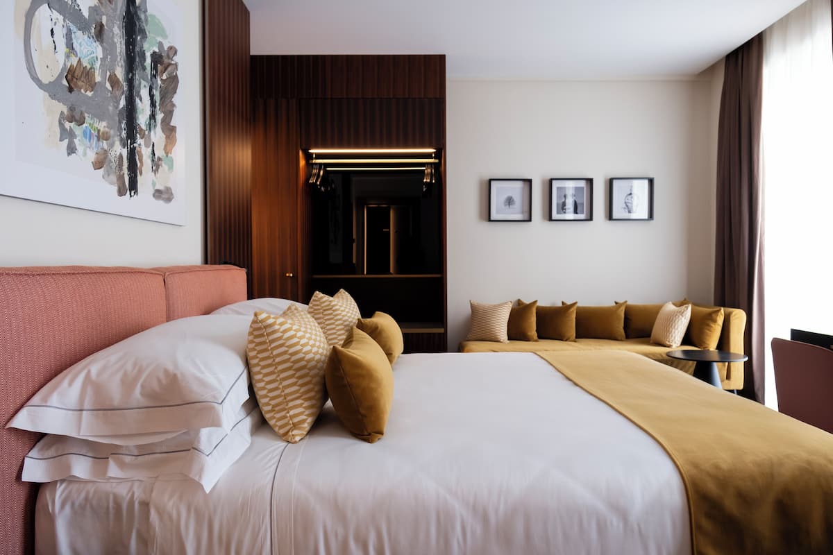 A hotel room with a large bed, a sofa, a TV, and a painting on the wall.