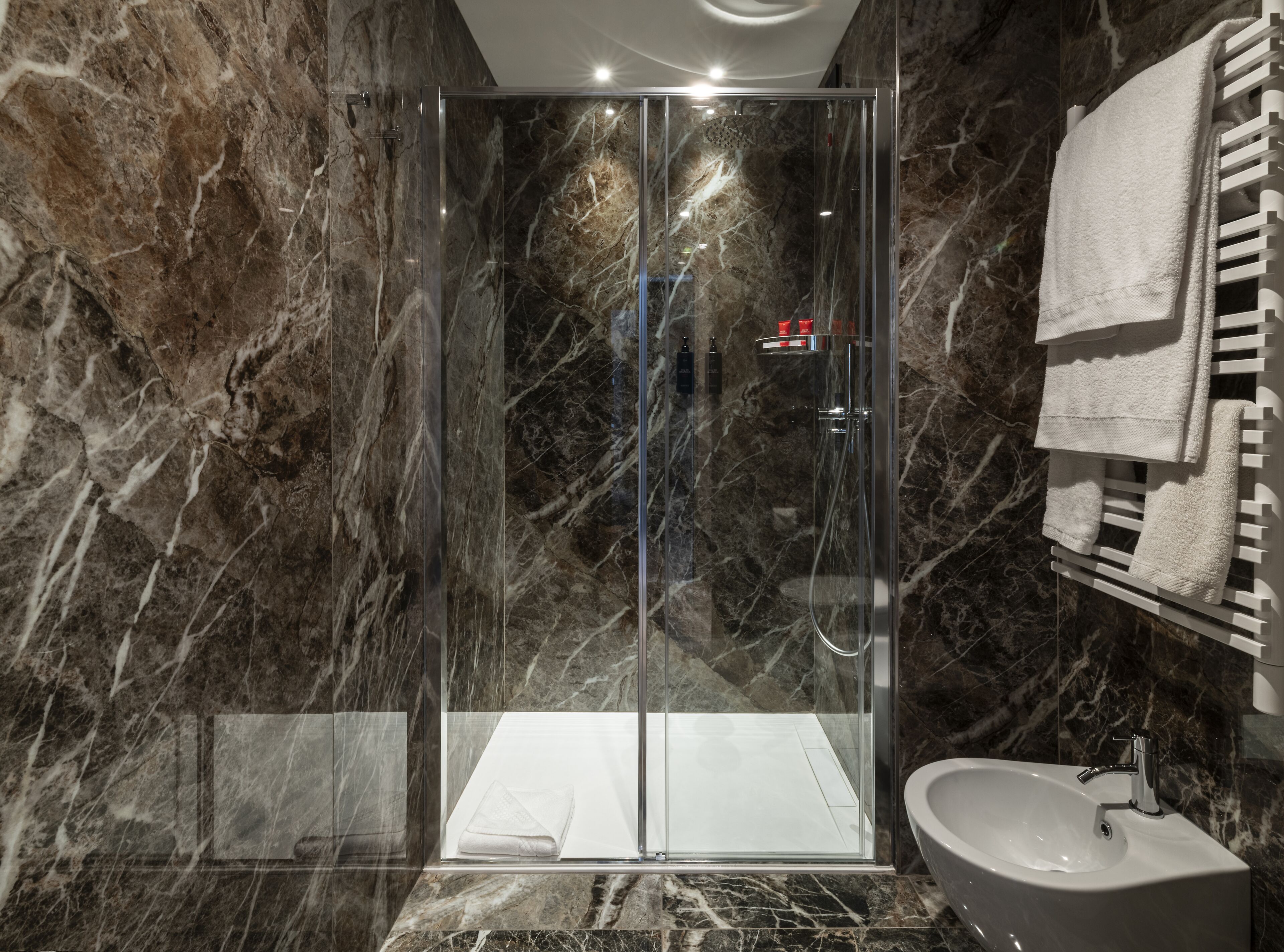 A modern bathroom with a glass-enclosed shower, marble walls, a sink, and a towel rack.