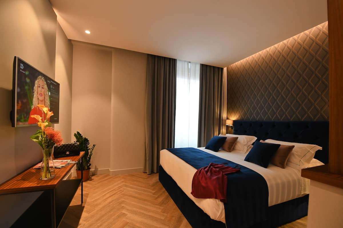 A modern hotel room with a large bed, a desk with a vase of flowers, and a painting on the wall.
