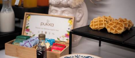 A table with a bottle of syrup, a box of tea, and a plate with waffles.