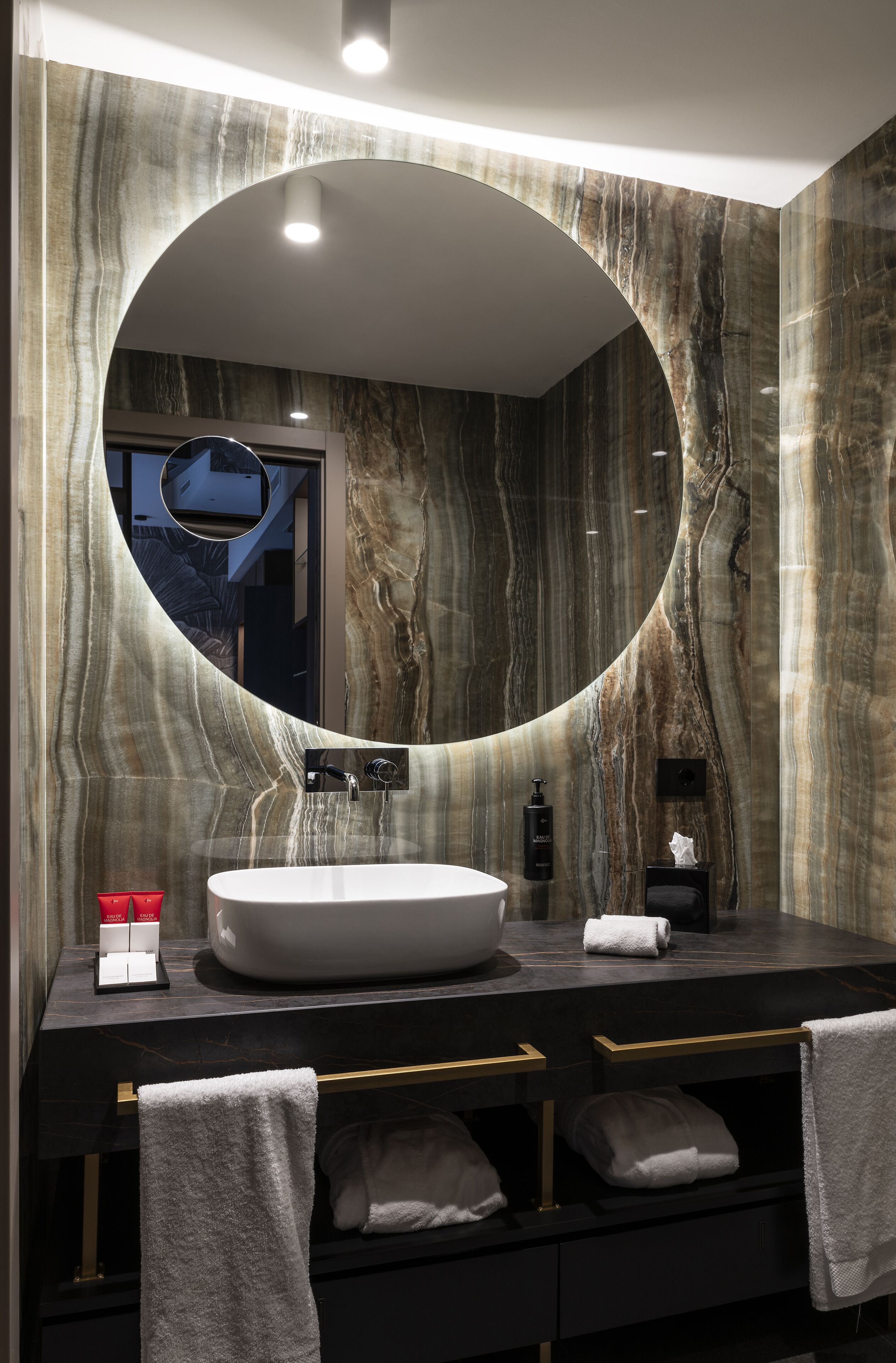 A modern bathroom with a large oval mirror, a white sink, and a dark marble countertop.