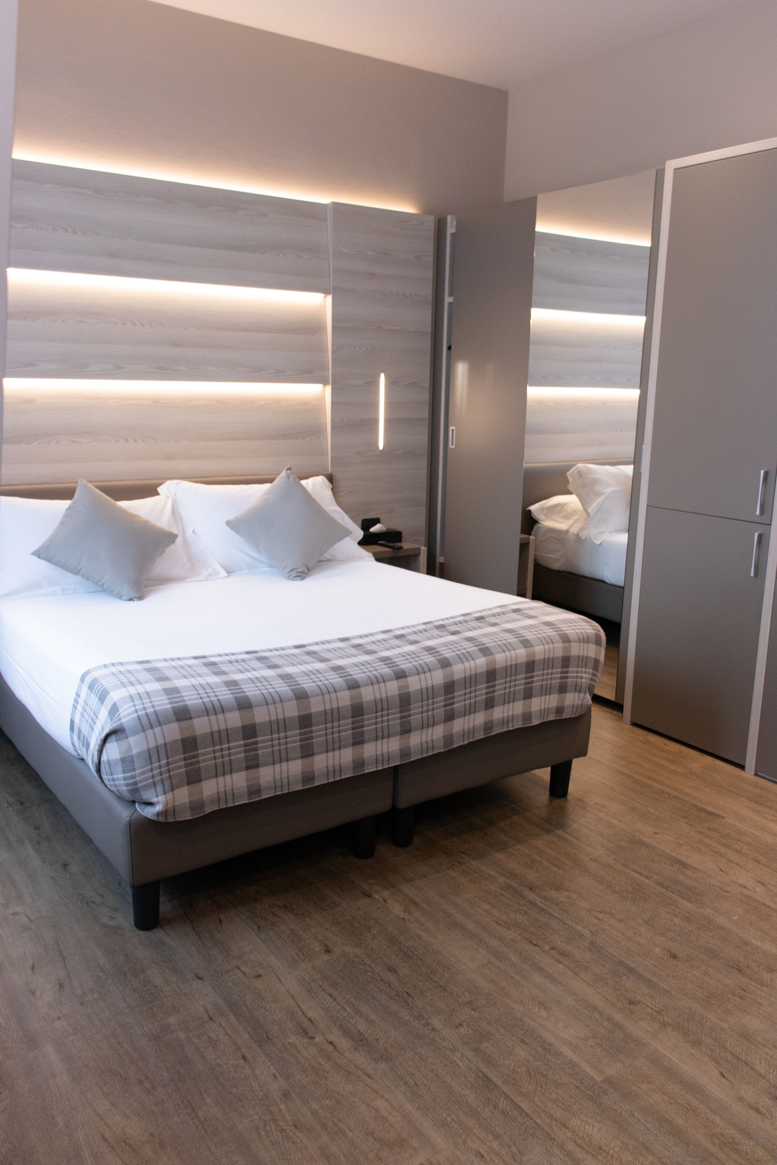 A modern bedroom with a large bed, bedside tables, a wardrobe, and built-in lighting.