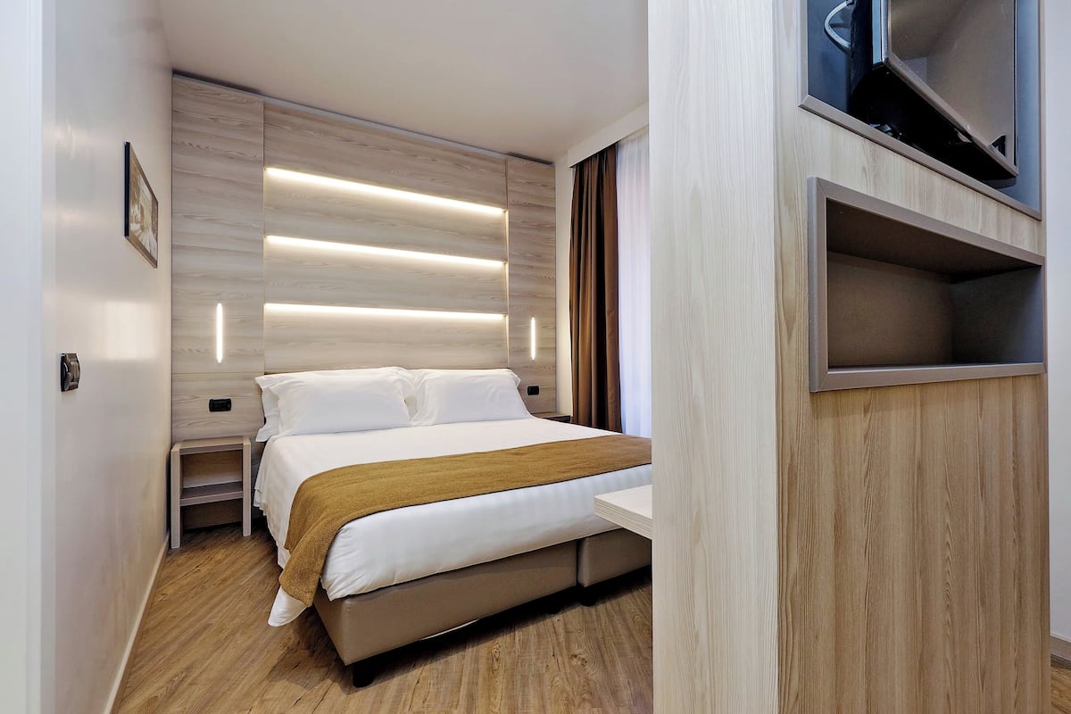 A modern hotel room with a bed, bedside tables, a TV, and a built-in shelf.