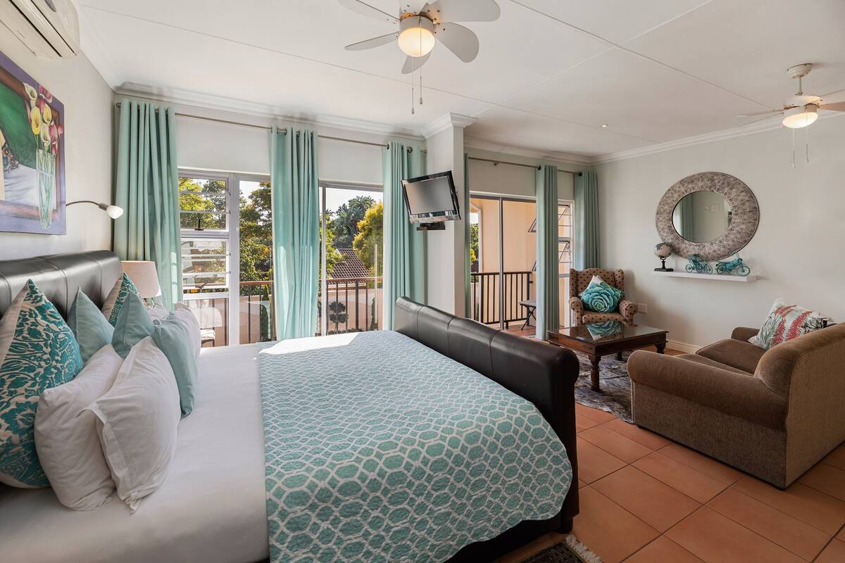 A bedroom with a bed, a sofa, a TV, and a balcony with curtains.