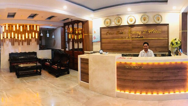 Zona de recepción de hotel con un mostrador de madera, un sofá y un reloj de pared.