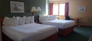 A hotel room with two beds, a desk, a chair, and two paintings on the walls.