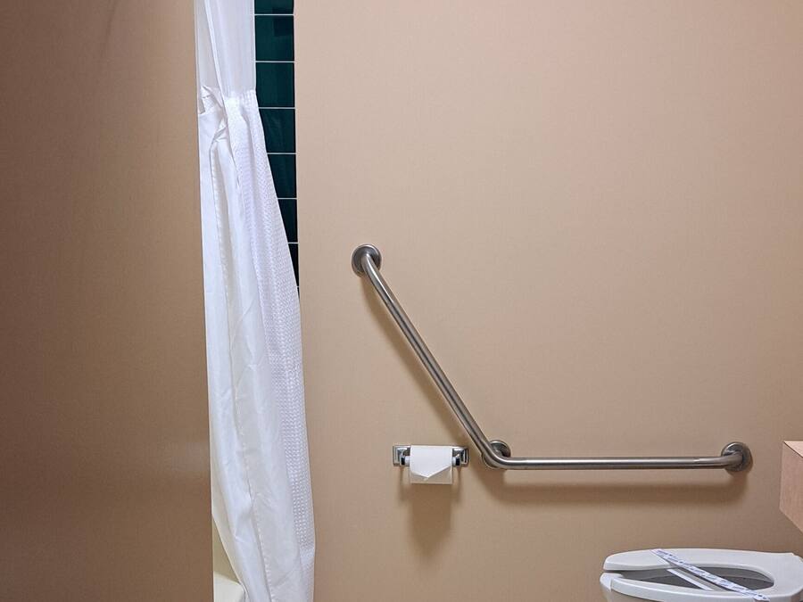 A bathroom with a toilet, a handrail, and a shower curtain.
