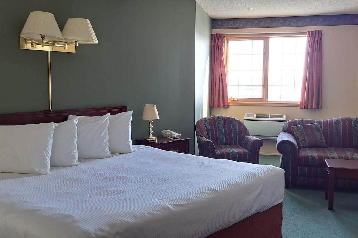 Une chambre d’hôtel avec un grand lit, deux fauteuils, un canapé, une petite table, une lampe et un tableau au mur.