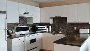 Een moderne keuken met witte kasten, een metselwerk spatwand en roestvrijstalen apparatuur.