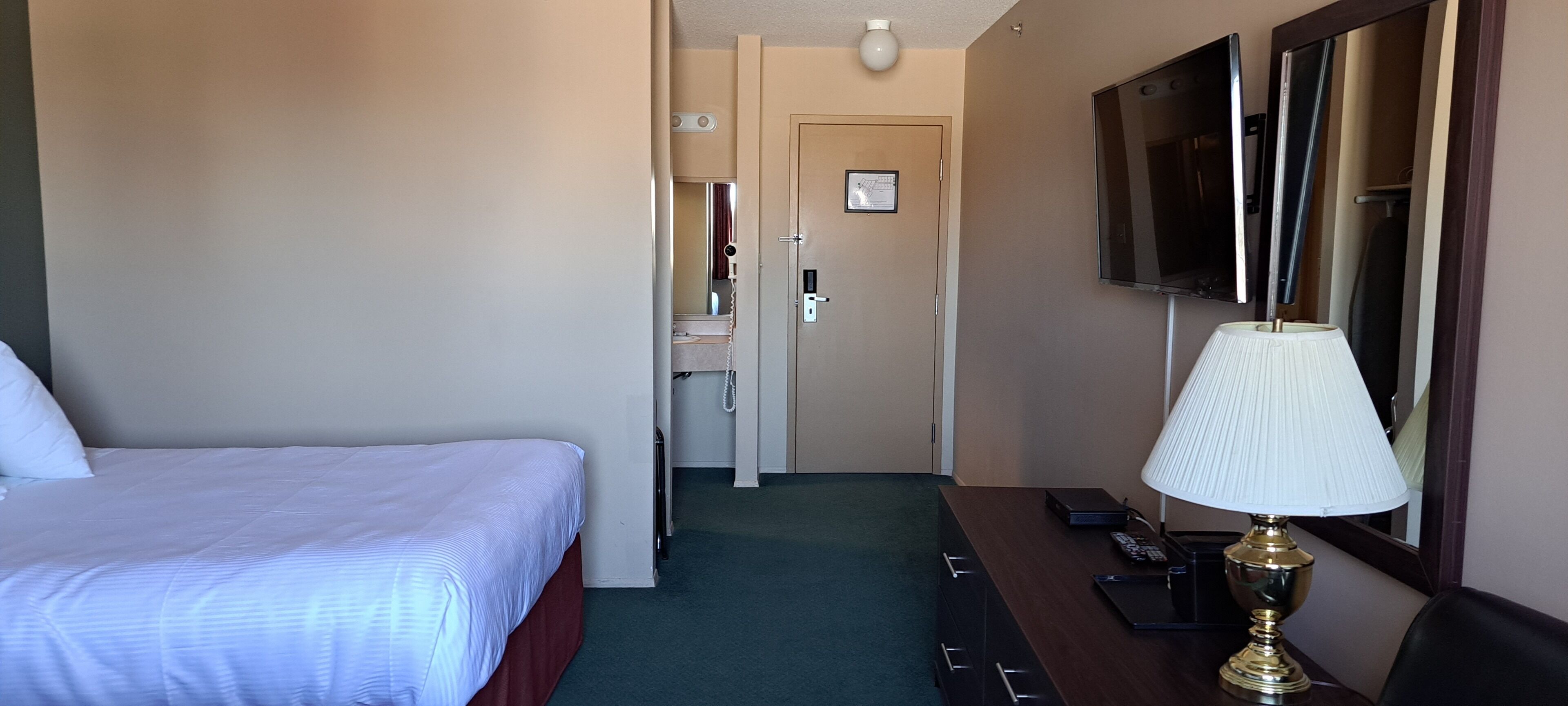 Ein Hotelzimmer mit Bett, Schreibtisch mit Lampe, Fernseher und einer Tür zum Badezimmer.