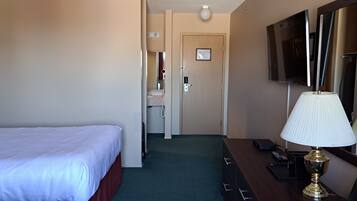 Ein Hotelzimmer mit Bett, Schreibtisch mit Lampe, Fernseher und einer Tür zum Badezimmer.