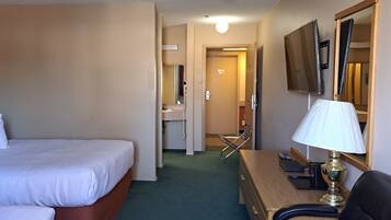 A hotel room with a bed, a desk with a lamp, a chair, and a bathroom visible through an open door.