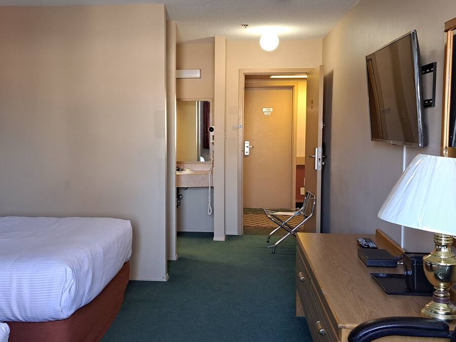 A hotel room with a bed, a desk with a lamp, a chair, and a bathroom visible through an open door.
