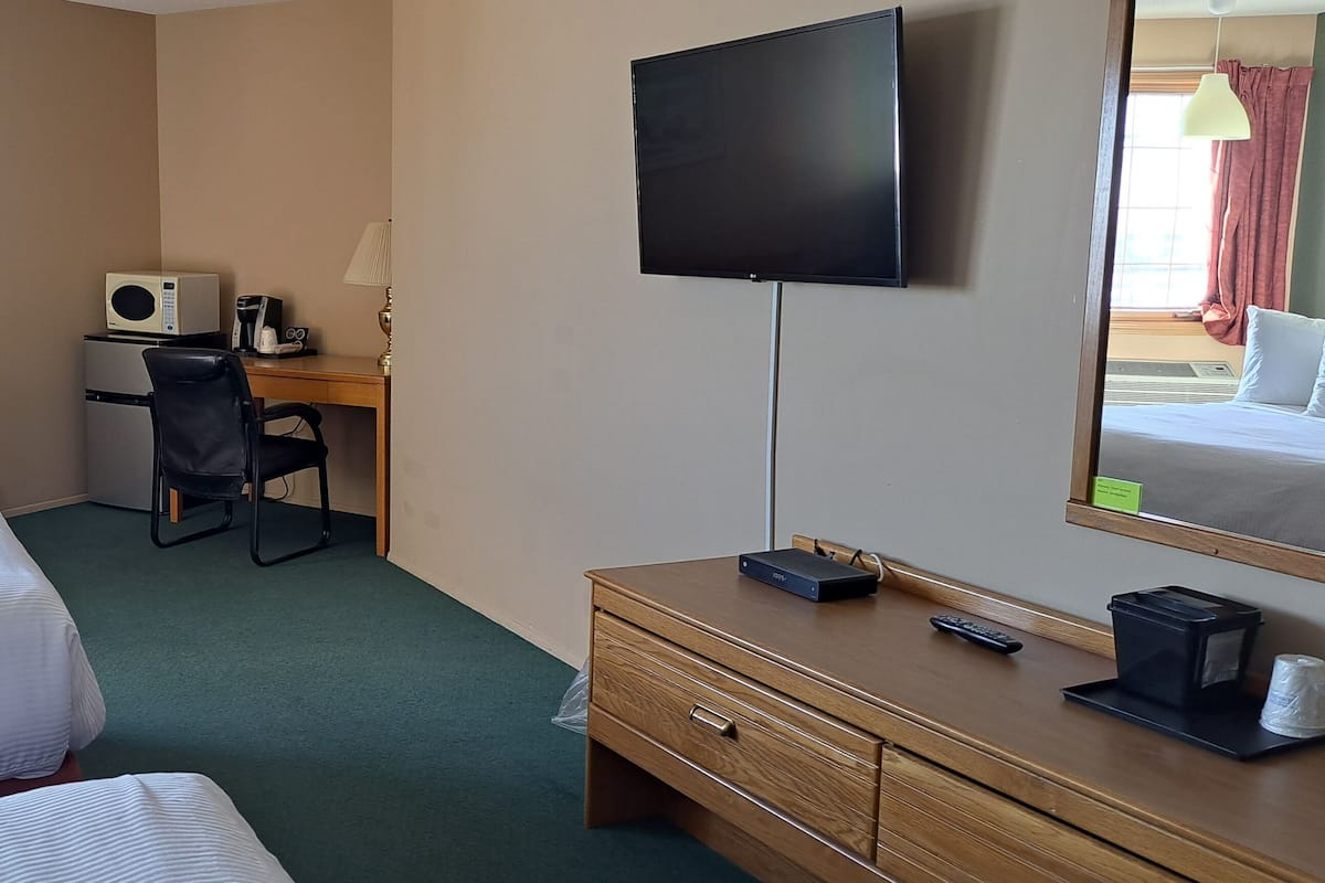 Une chambre d’hôtel avec deux lits, un bureau avec un ordinateur, une télévision et une petite table.